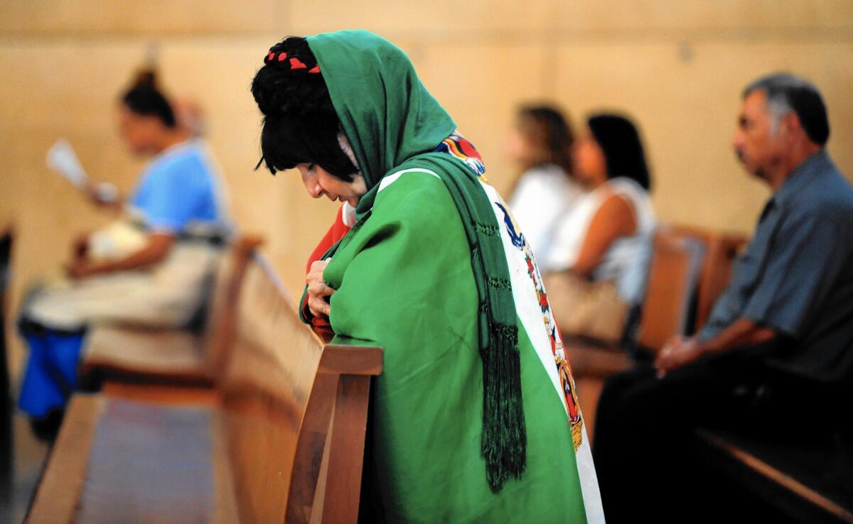 A woman wrapped in a Mexican flag with the Virgin Mary on it prays at the Cathedral of Our Lady of the Angels in downtown Los Angeles.