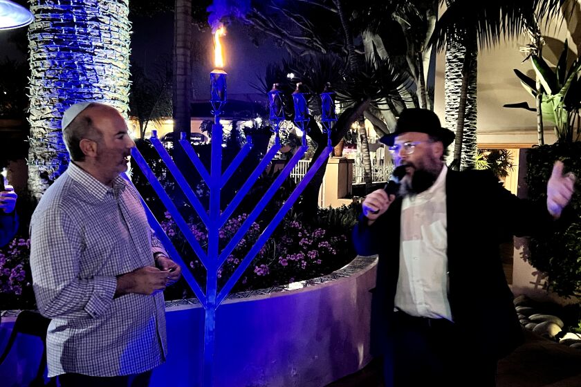Rabbi Baruch Ezagui (right) speaks as Carlos Wellman prepares to light three torches on the menorah at the La Valencia Hotel.