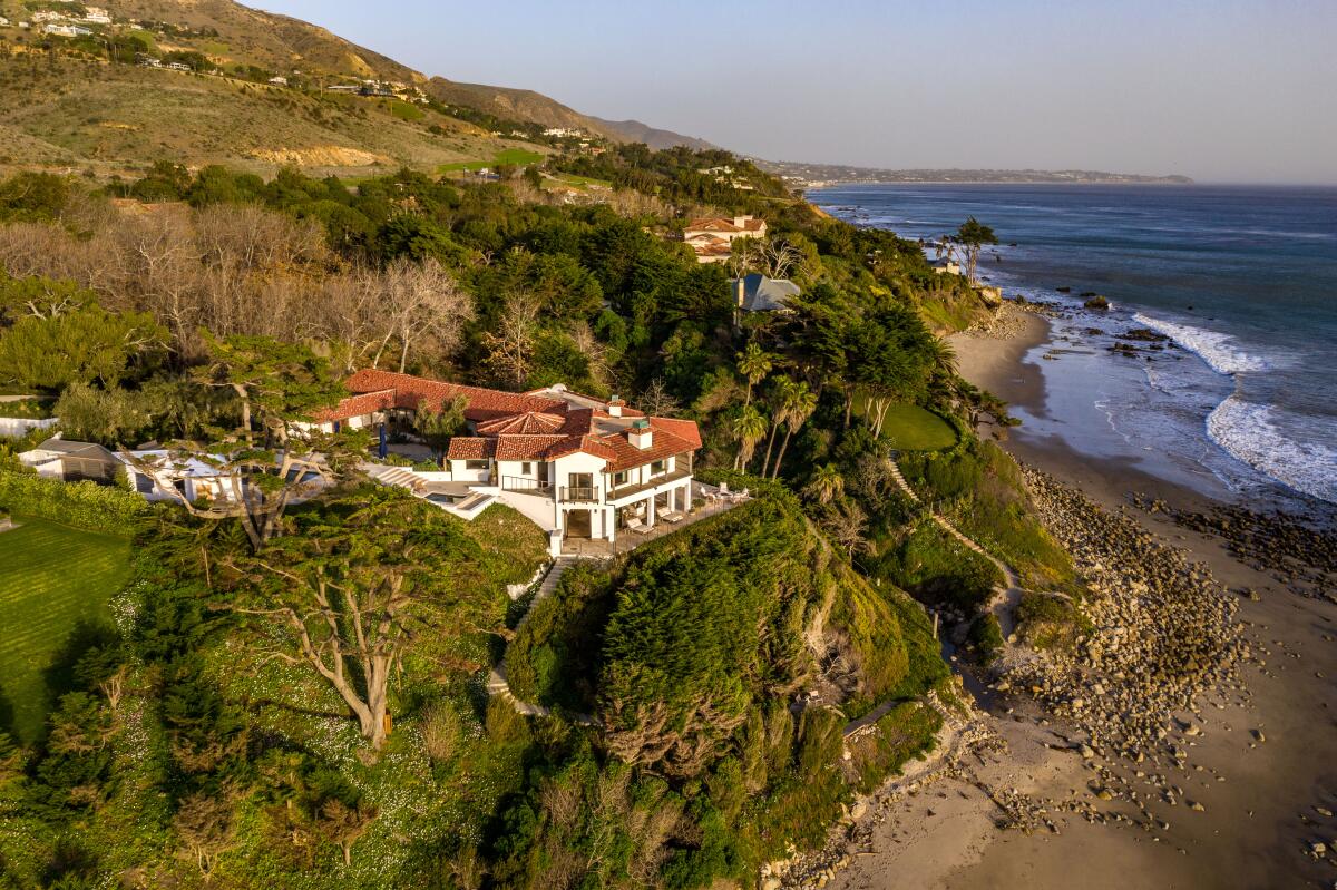 A mansion built on a bluff overlooks a beach.