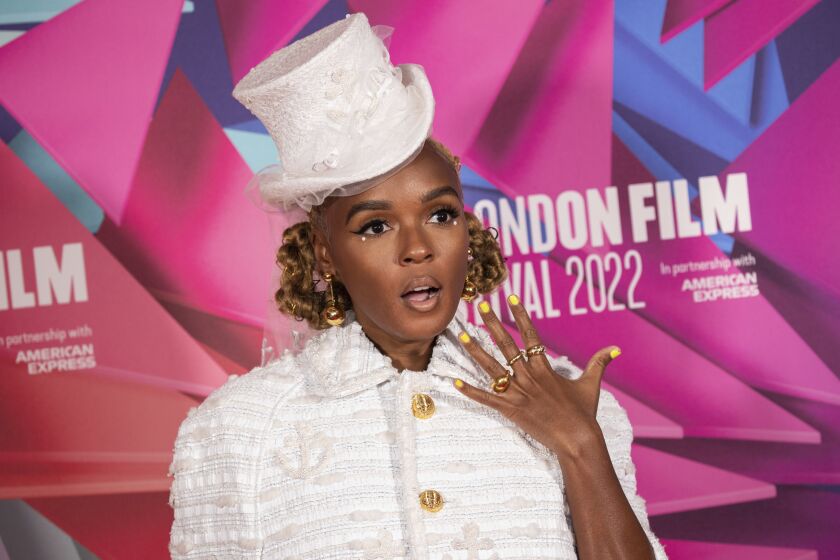 A person with brown braided hair wearing a white top hat and matching coat while posing with their mouth agape