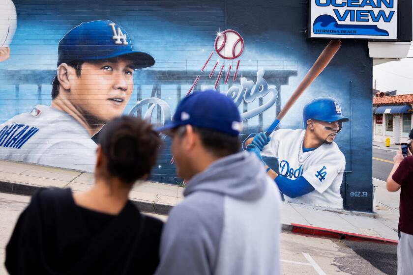HERMOSA BEACH-CA-DECEMBER 19, 2023: People stop to take photos of a mural featuring newest Dodger player Shohei Ohtani, left, and Mookie Betts, right, by artist Gustavo Zermeno, Jr. on the side wall of Ocean View Liquor store in Hermosa Beach on Tuesday, December 19, 2023. (Christina House / Los Angeles Times)