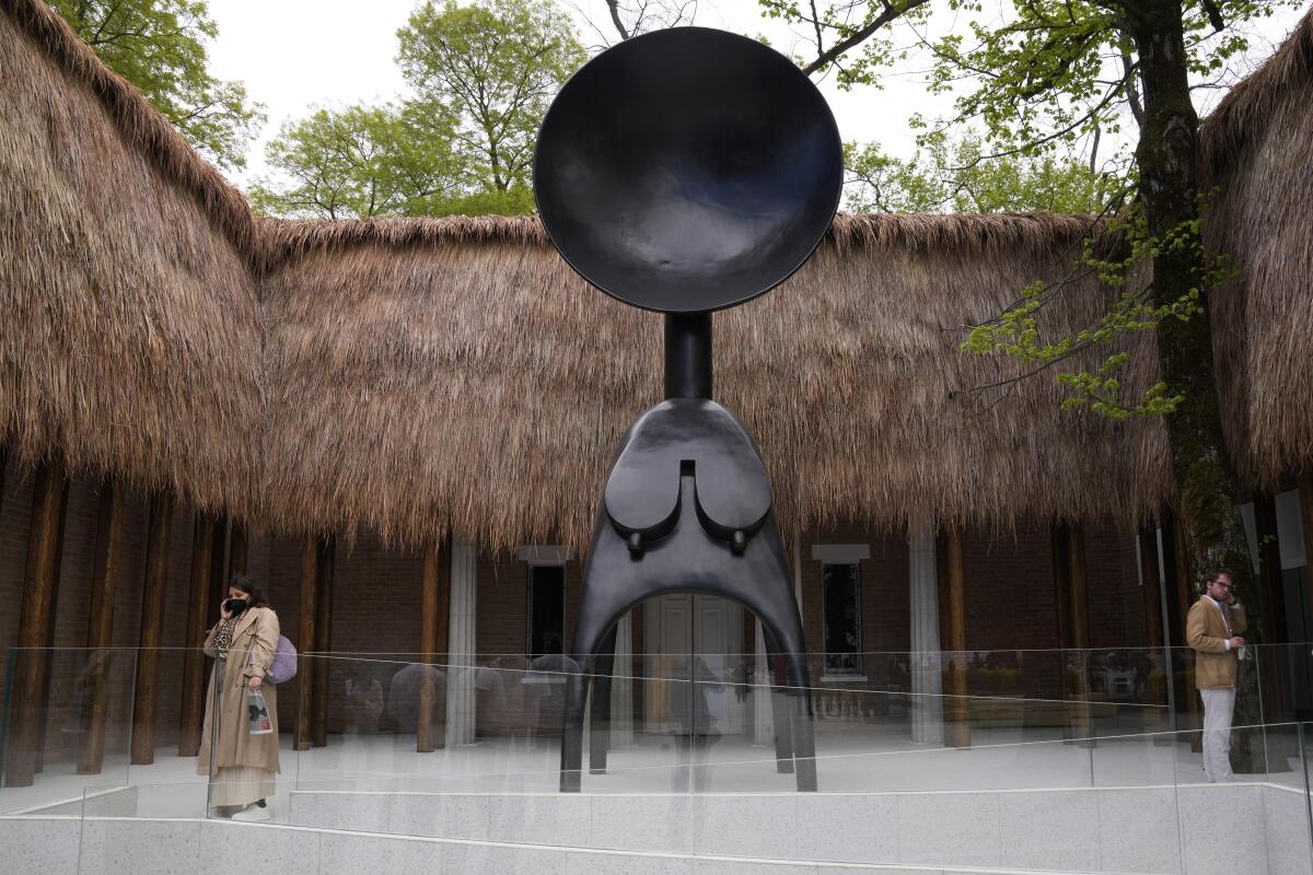 A towering Simone Leigh sculpture inspired by a West African ritual mask in a courtyard with thatch on its roof.