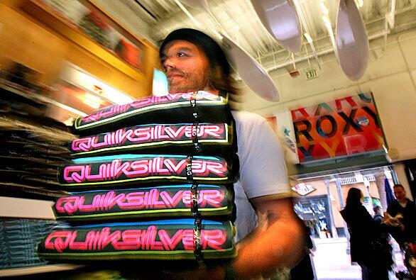 Sales associate Chad Markowitz carries a stack of shirts at Huntington Surf & Sport. With surfers cutting back on new surfboards, wetsuits and board shorts, executives and workers at surf goods stores are holding their breath.