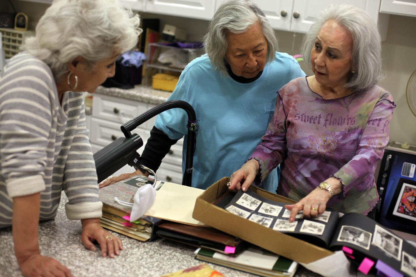 Teresa Montelongo, left, Yuri Long and Sumi Hughes look at old photos of themselves and their families at Hughes' home. The Atomettes celebrate the 65th anniversary of their social group this year.