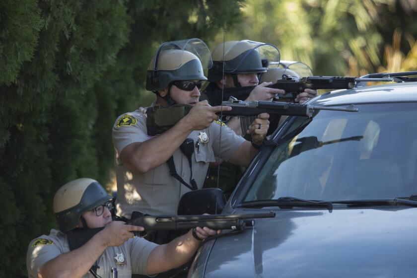 San Bernardino County sheriff's deputies draw guns behind a minivan on Richardson St. during a search for suspects involved in the mass shooting of 14 people at the Inland Regional Center in San Bernardino.