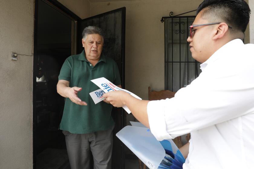 EAST LOS ANGELES, CA -- FEBRUARY 27, 2020: Ricardo Alonzo, right, a volunteer with the Bernie Sanders campaign, hands out bumper stickers to Rudolfo Anguiano who says his household is four Sanders voters -- him, his wife, daughter and niece. Alonzo says he does not try to convert voters while he is canvassing but instead shares information about his candidate. (Myung J. Chun / Los Angeles Times)