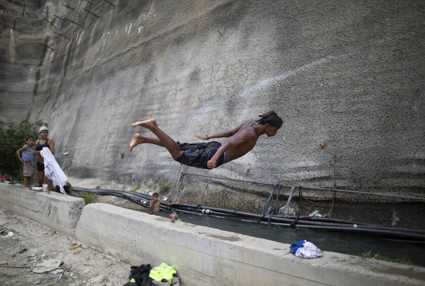 A youth dives into a drainage ditch alongside an unfinished, abandoned highway in Caracas, Venezuela, on Thursday, July 15, 2021. Residents directed tubes toward the drainage ditch to fill it with water coming from a nearby mountain in order to do laundry, bathe and collect water to take home, while children use it as a pool. (AP Photo/Ariana Cubillos)