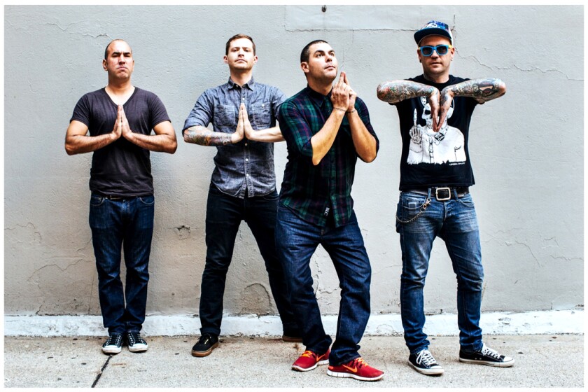 Four guys stand against a wall, with hands in prayer formation