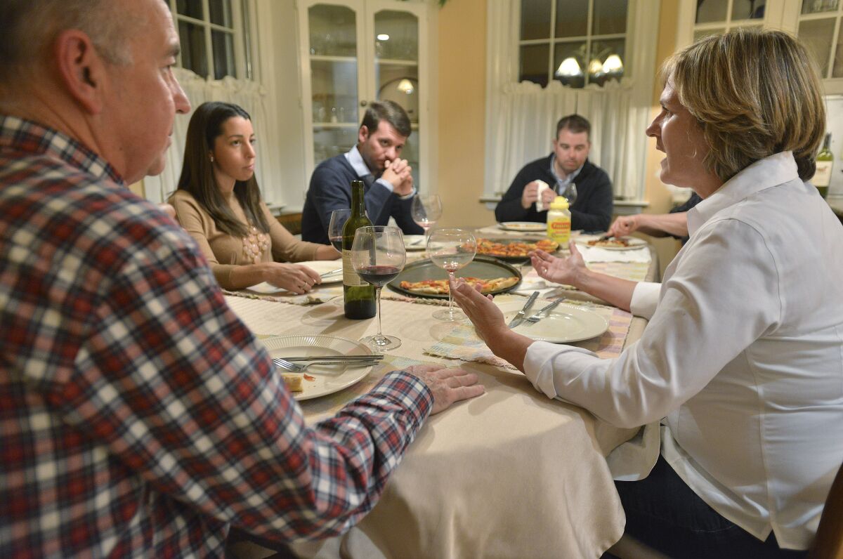 Five people, members of a family, sit around a dinner table discussing politics. 