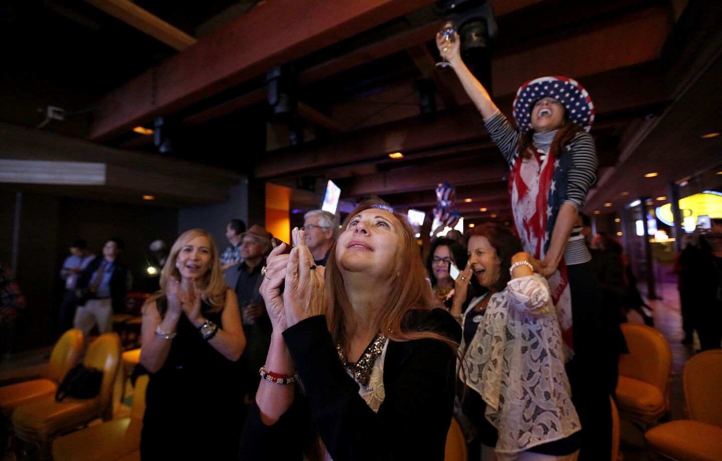 Republicans Enrietta Lee, center, prays, as Sarah McDowell, right, celebrates at the OCGOP election party at China Palace in Newport Beach after the election of Donald Trump as president.