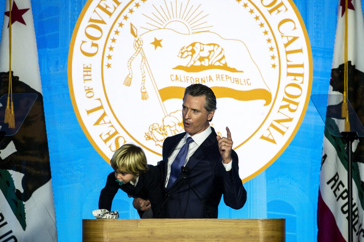 Gov. Gavin Newsom speaks while holding his youngest son, Dutch