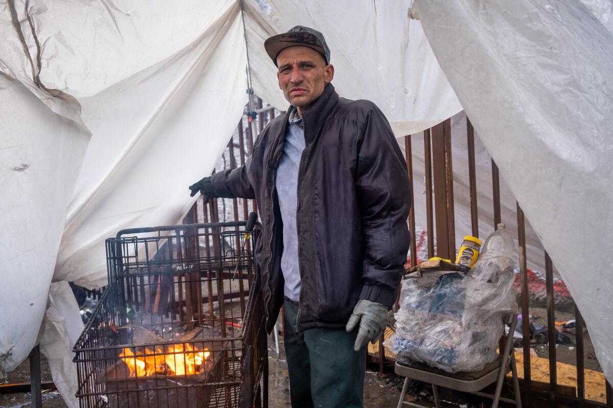 A man stands next to a fire in a grocery cart.