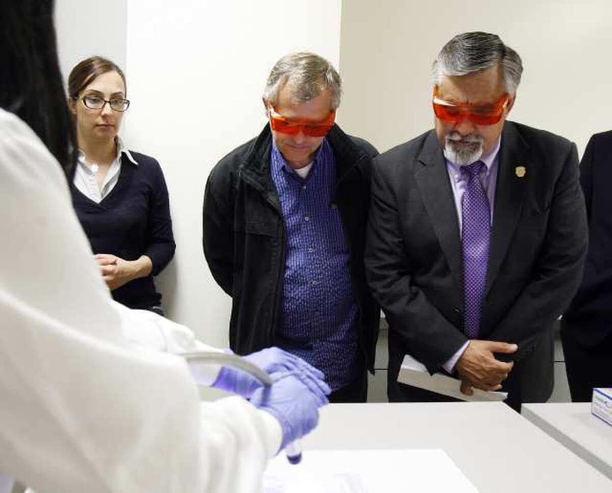 Burbank Mayor Jess Talamantes, right, wears orange glasses to see fluid evidence during a demonstration at the opening of the Verdugo Regional Crime Laboratory in the Glendale Police Department on Thursday. The lab is a tri-city partnership with Glendale, Burbank and Pasadena, and the ATF also partnered.