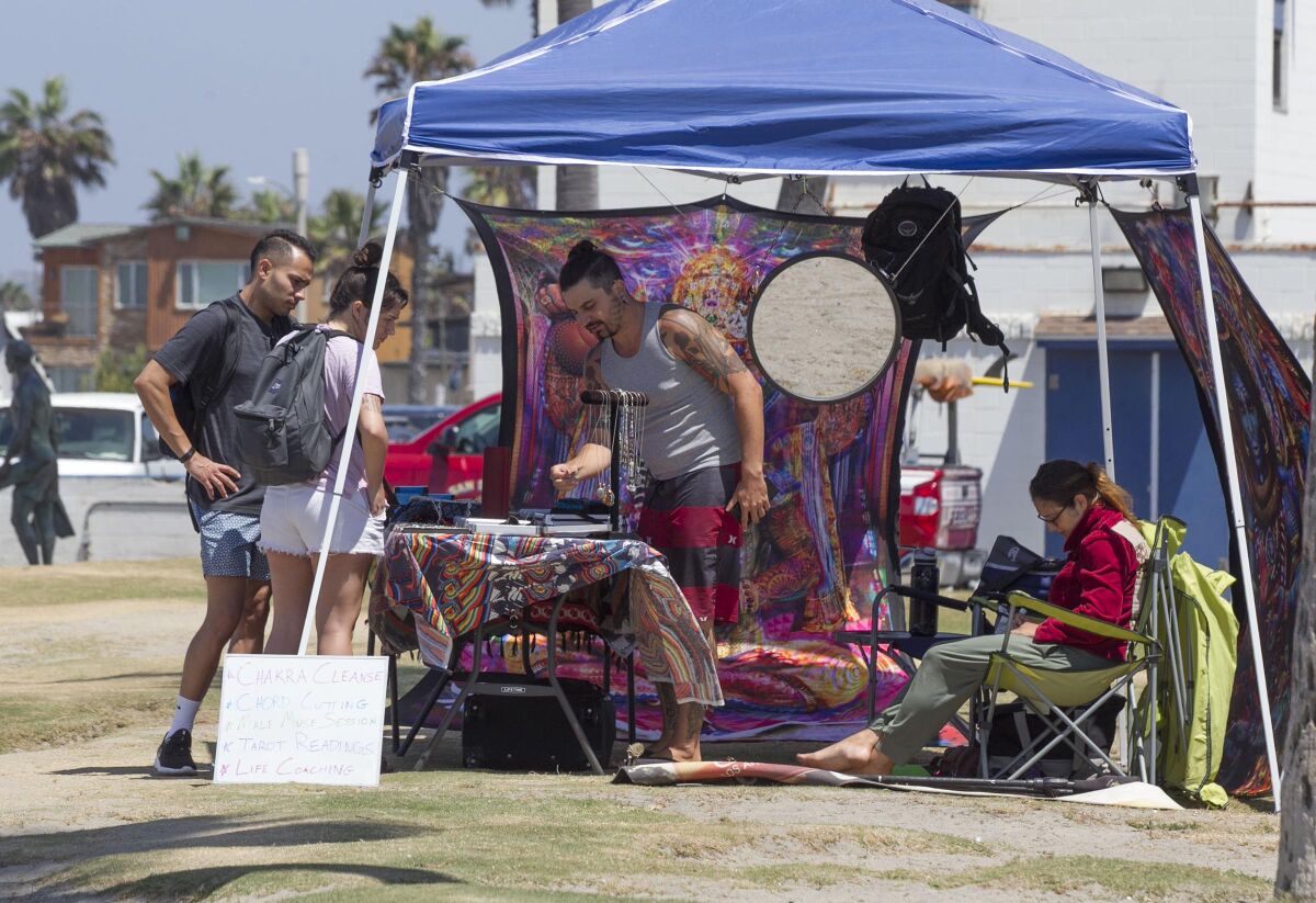 People look at jewels and crystals being sold by a street vendor in Ocean Beach in 2019.