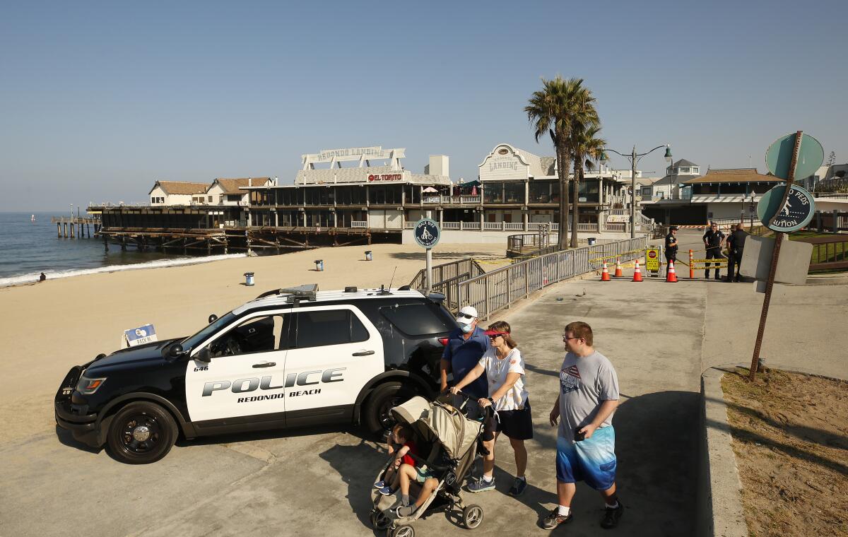 People walk past a black and white SUV with the words "Police Redondo Beach" on its doors.
