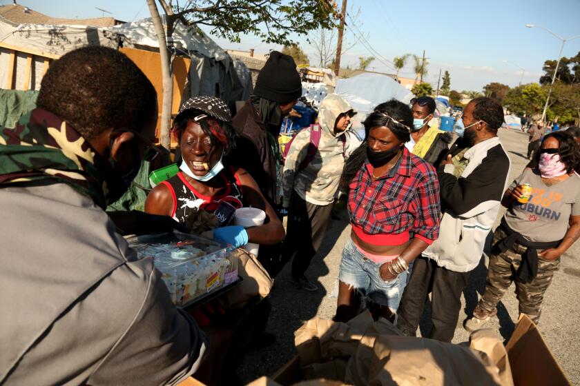 LOS ANGELES, CA - APRIL 11, 2020 - Gernay Quinnie, 38, left, with Reclaiming America's Communities through Empowerment (R.A.C.E.) helps feed the homeless who live in a vacant parking lot in South Los Angeles on April 11, 2020. Possibly 50 people live homeless at the site. Quinnie and fellow workers with R.A.C.E. also give the homeless hygiene bags which includes, toiletries, hand sanitizers, masks and gloves to help protect them during the coronavirus pandemic. Quinnie, with the South LA-based gang intervention organization, is also risking his own health: he suffers from an immune disorder. "If i don't go out, who else is going to do it," he said. (Genaro Molina / Los Angeles Times)