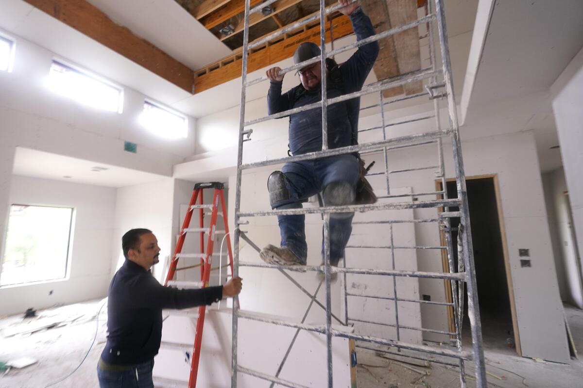 Joshua Correa, izquierda, afirma un andamio para un trabajador en una casa en construcción
