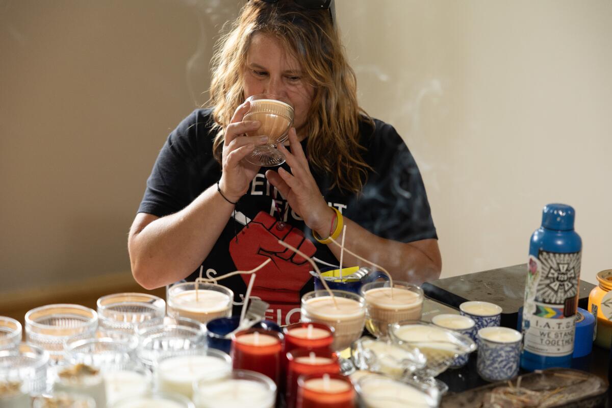 A seated woman sniffs one of a number of candles arrayed before her