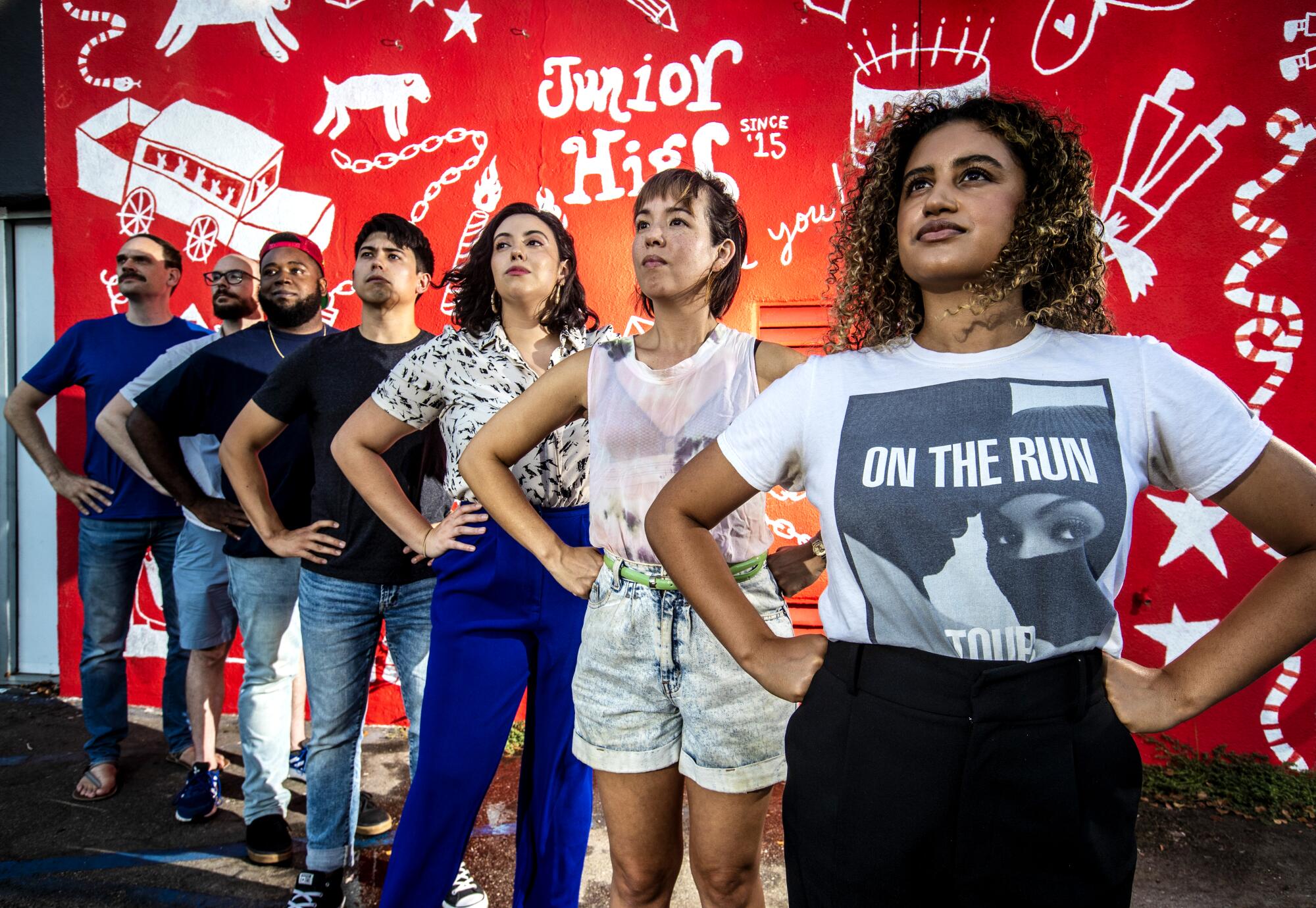 Seven people stand in a line with their hands on their hips