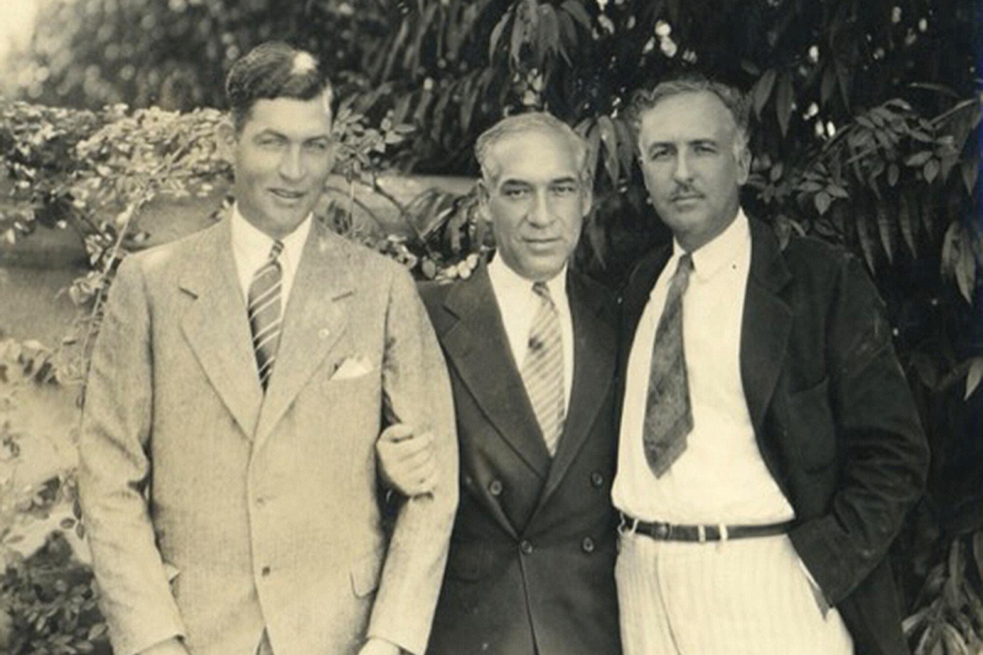 Three men in suits, standing outdoors, in a vintage black-and-white photo.