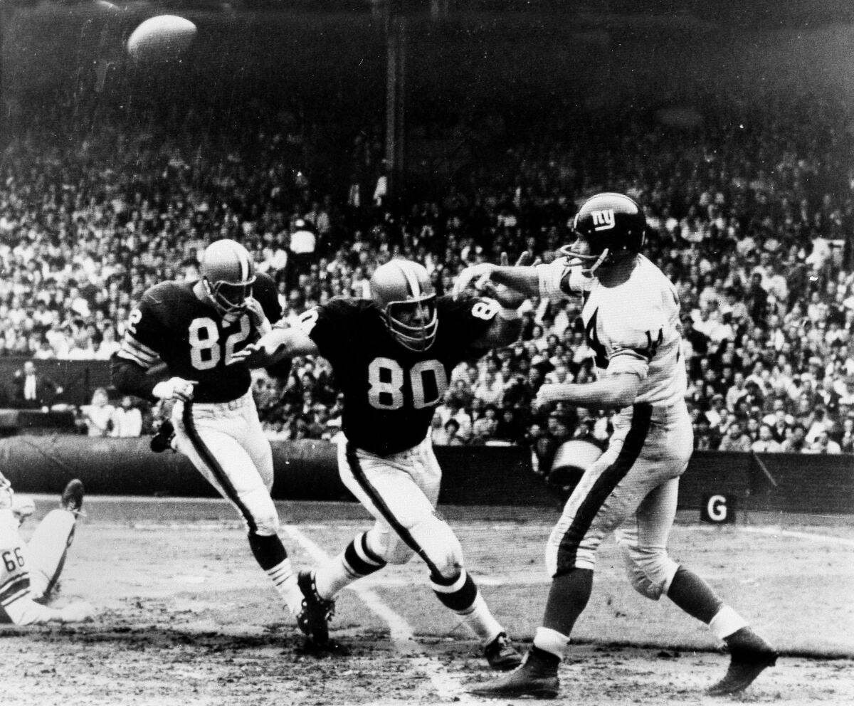 FILE - Cleveland Browns' Bill Glass (80) rushes towards New York Giants' quarterback Y.A. Tittle after he threw a pass during the first quarter of a football game in Cleveland, Oct. 27, 1963. Bill Glass, a four-time Pro Bowl defensive end with Cleveland and member of the Browns' 1964 NFL championship team, has died. He was 86. The Browns said Glass died Sunday night, Dec. 5, 2021, surrounded by family at his home in Waxahachie, Texas.(AP Photo/File)