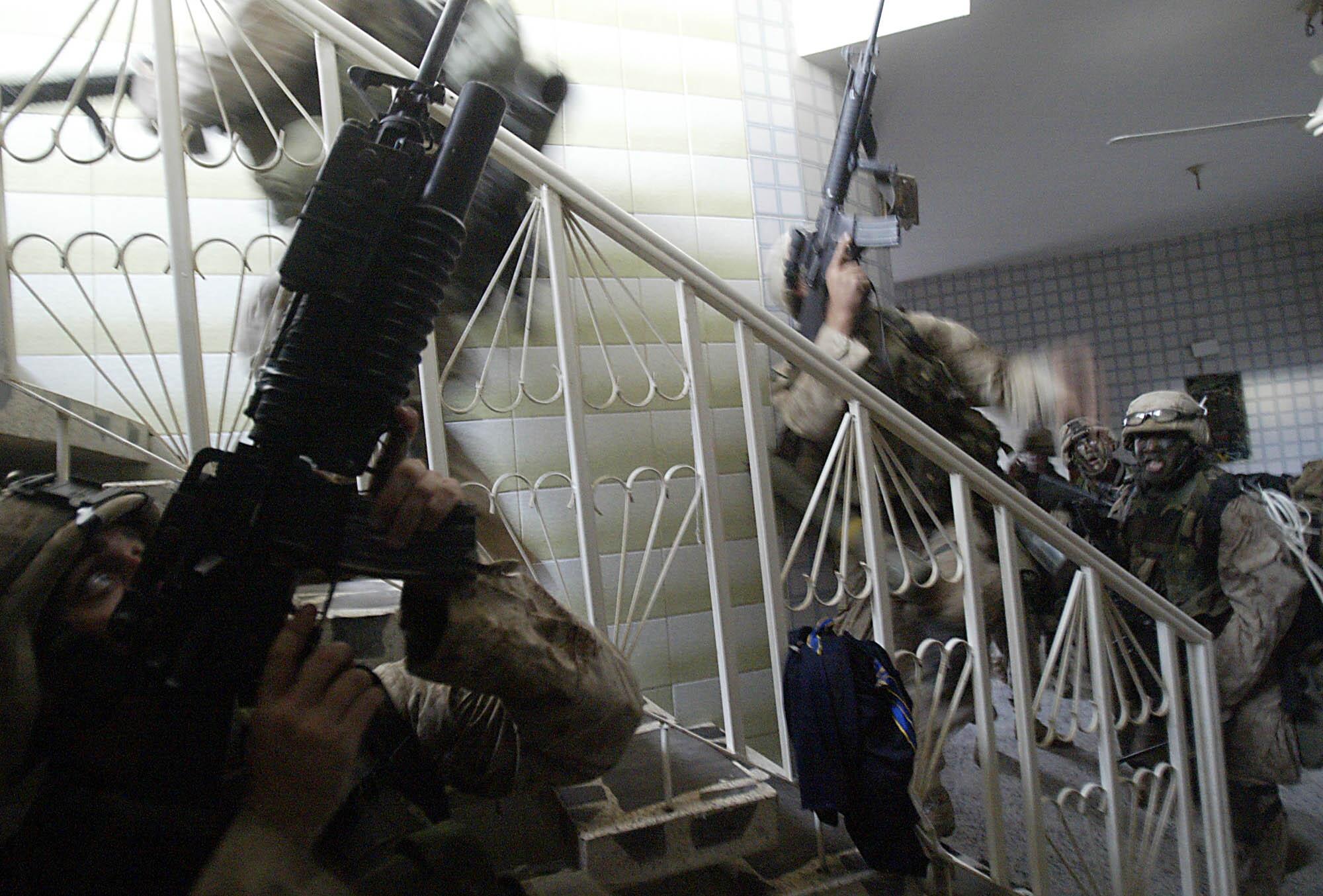 Marines point guns upward in a house