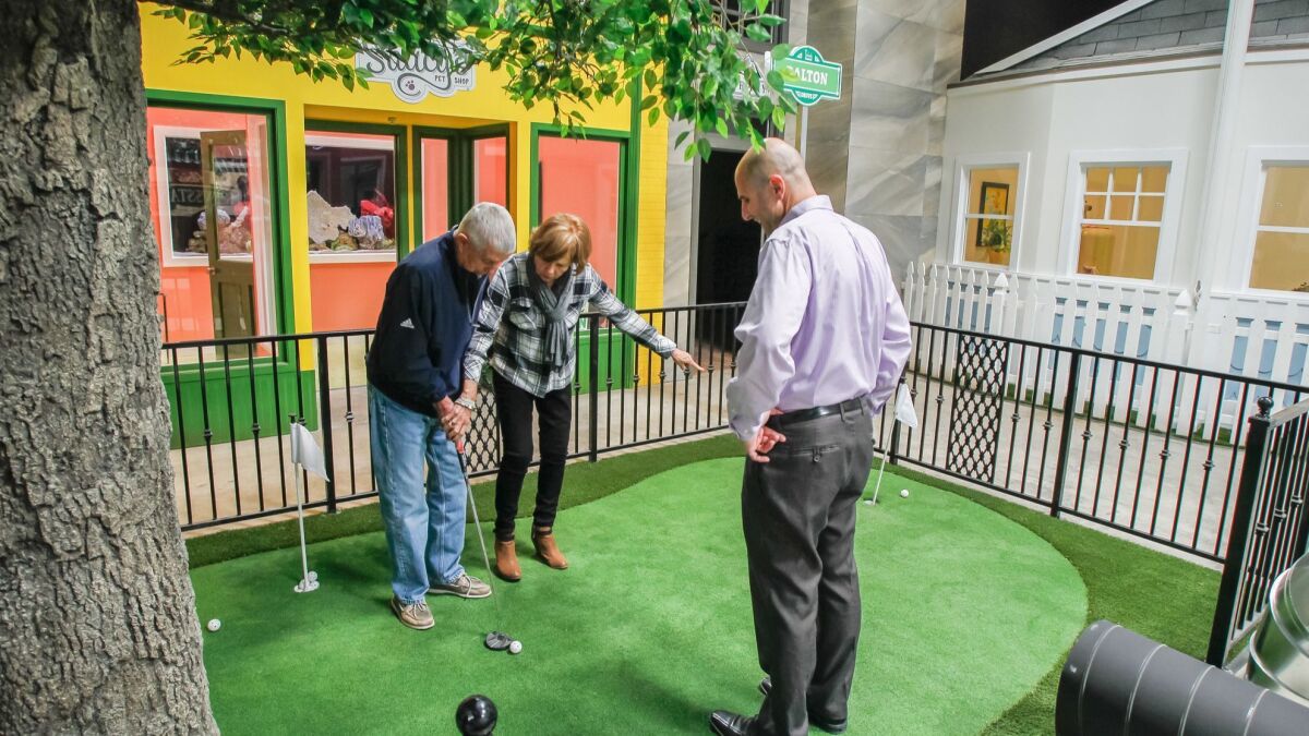Glenner Town Square founder Scott Tarde, right, watches Bonita resident Sue Foley guides her husband, Bill, on the putting green. Glenner Town Square, a miniature memory village for Alzheimer's patients like Bill, will soon open inside a Chula Vista industrial building.