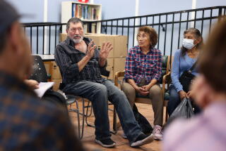 A man gestures with both hands as he speaks during a discussion with others, their chairs in a circle