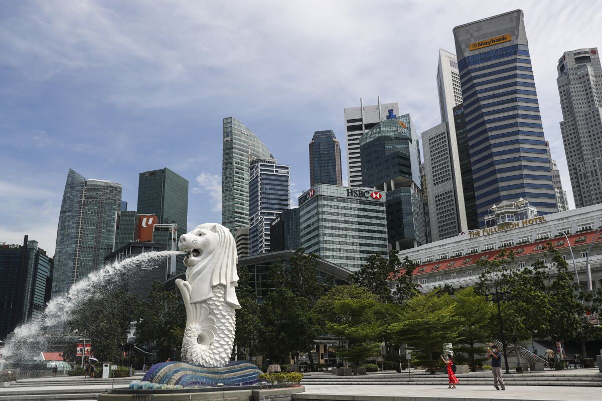 FILE - People are dwarfed against the financial skyline as they take photos of the Merlion statue along the Marina Bay area in Singapore, Tuesday, June 30, 2020. Singapore's president has ordered a delay in the execution of two men sentenced to death who are believed to be mentally disabled, a lawyer said Thursday, Feb. 17, 2022. (AP Photo/Yong Teck Lim, File)