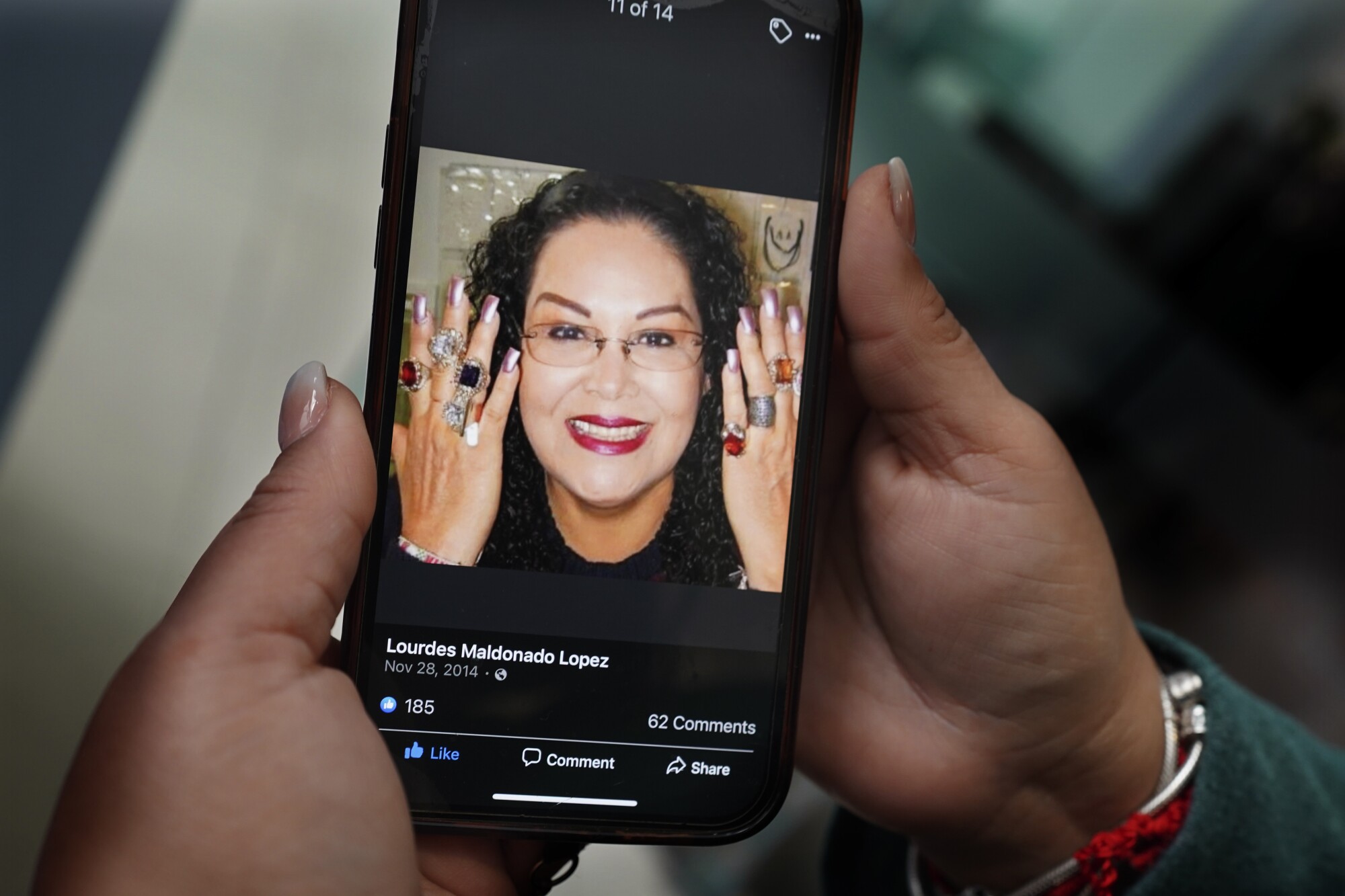 A woman holds a mobile phone with a smiling picture of Lourdes Maldonado 
