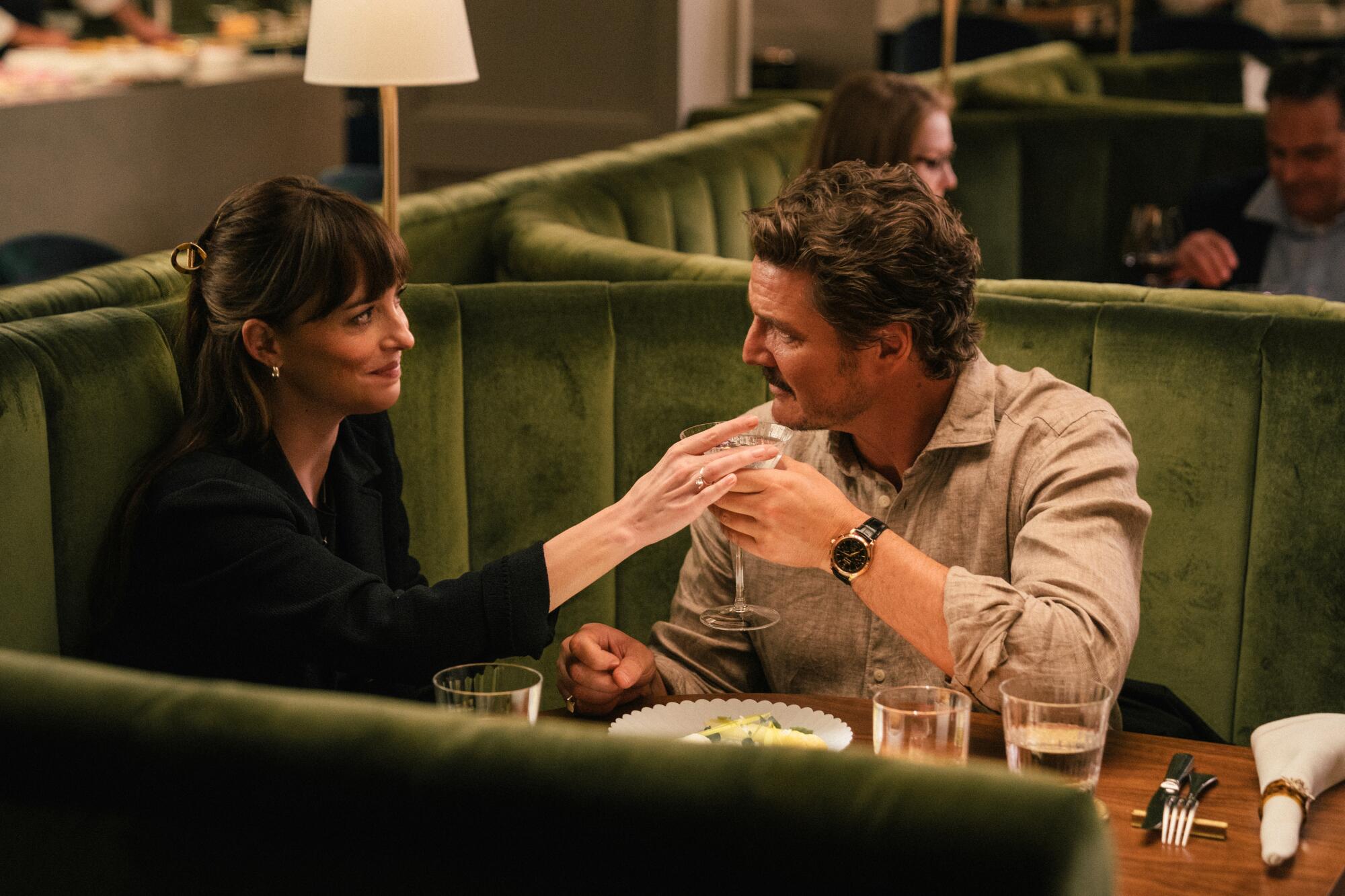 A man and a woman sit in a dark green booth in a restaurant.