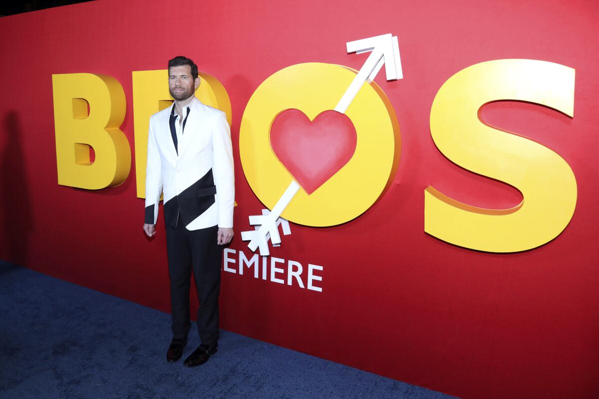 A man in a white blazer stands in front of a large sign that says "Bros."