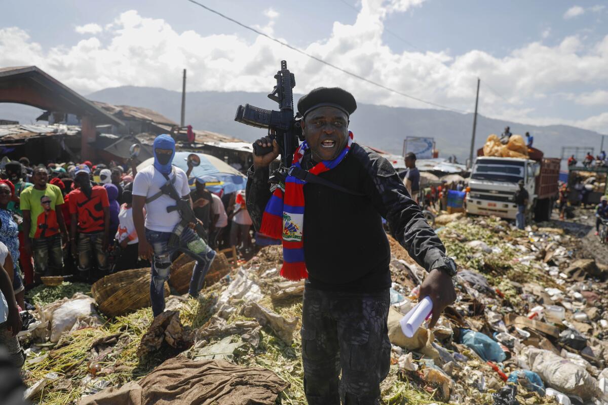 A man holding a rifle and several other people stand next to garbage. 