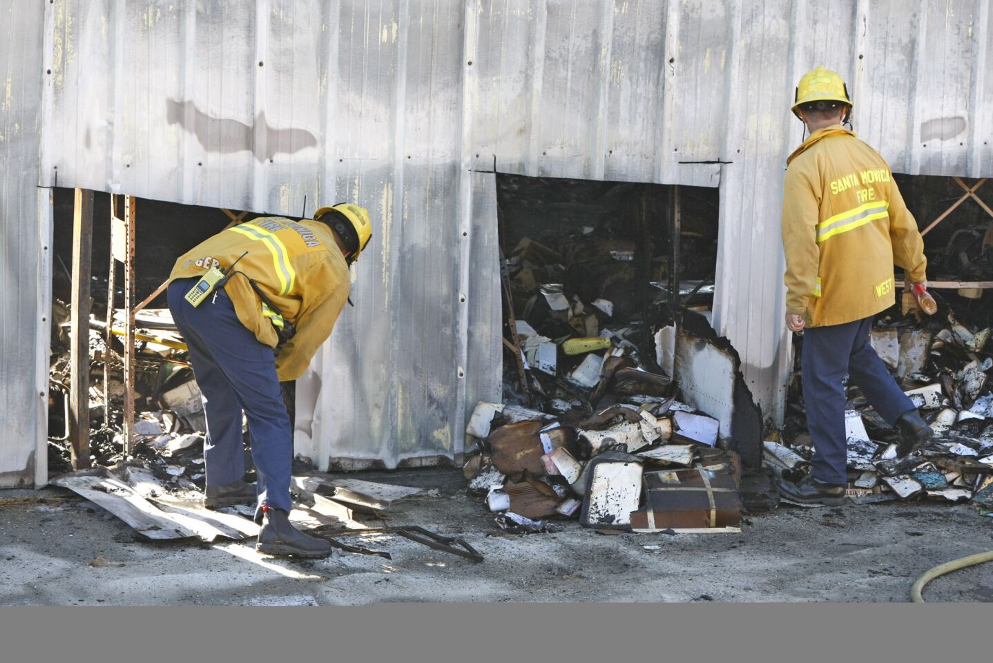 Santa Monica firefighters look through burned debris at the back side of an aircraft hangar where a private jet crashed and burned Sunday evening.