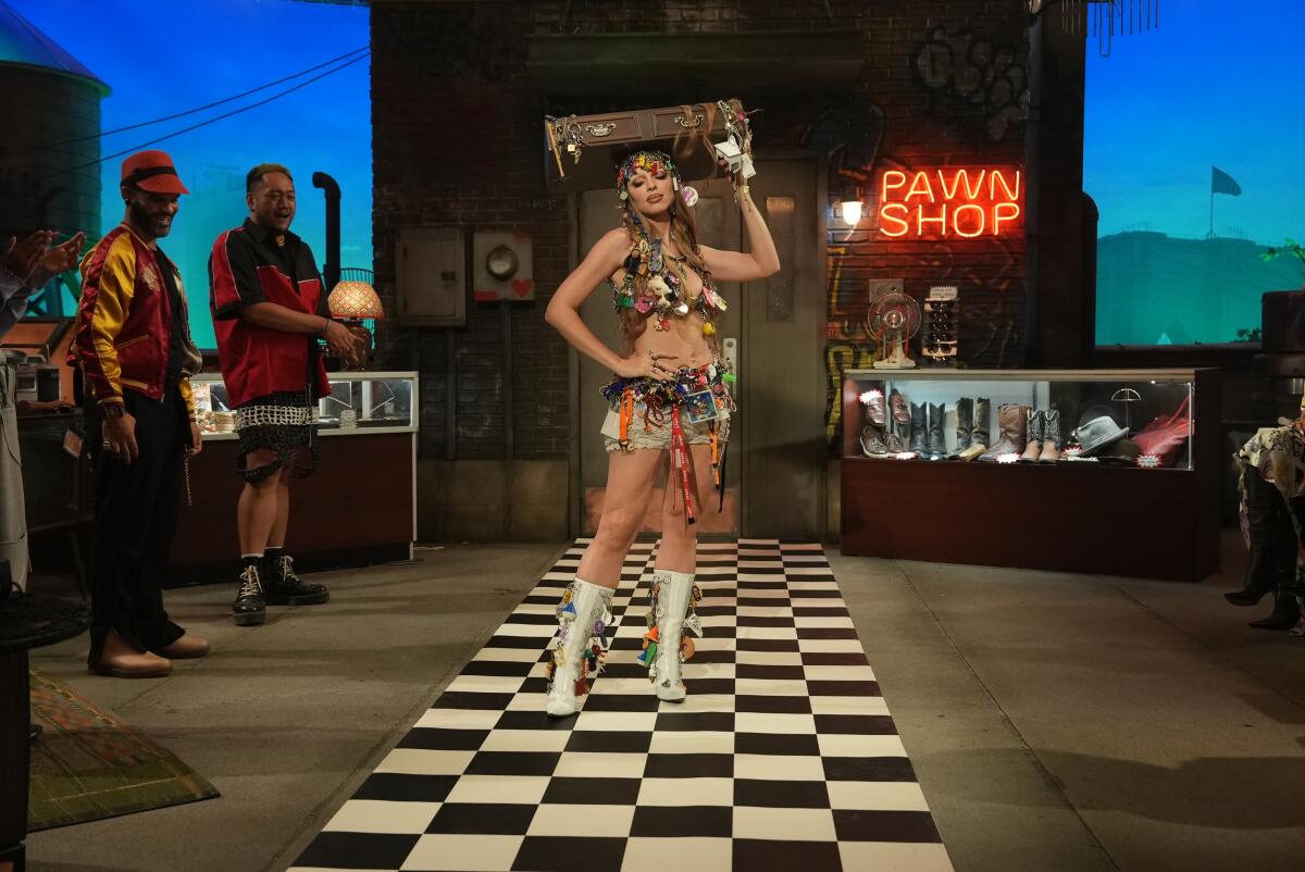 A woman in a halter top and miniskirt adorned with knickknacks holds a drawer on her head.