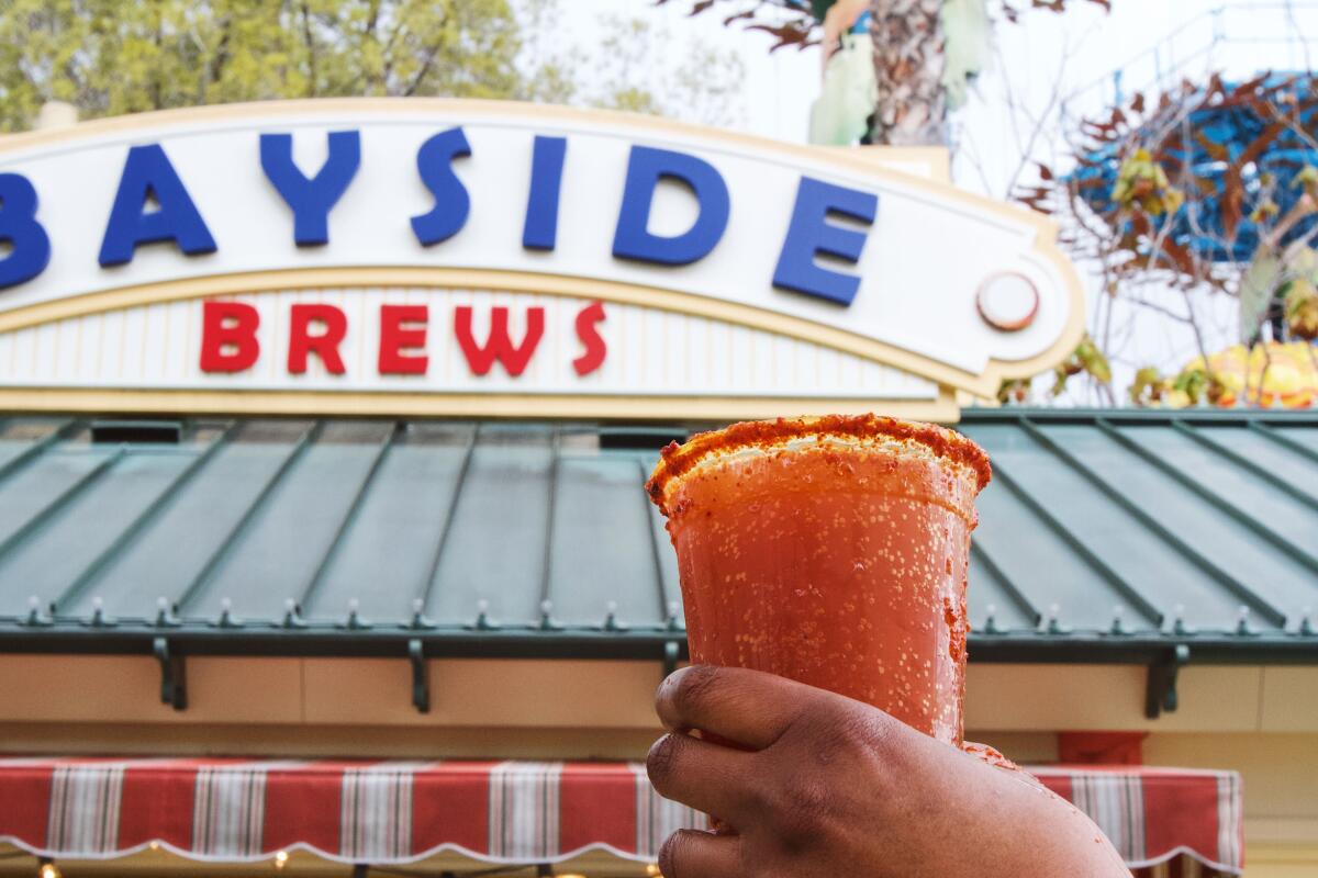 A hand holds a a red drink up toward a sign that says Bayside Brews.