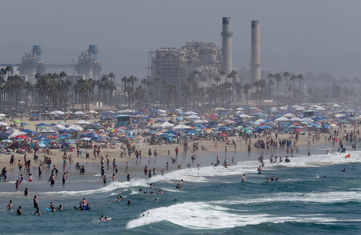 Crowds in Huntington Beach during a triple-digit heat wave, with a gas-fired power plant in the background.