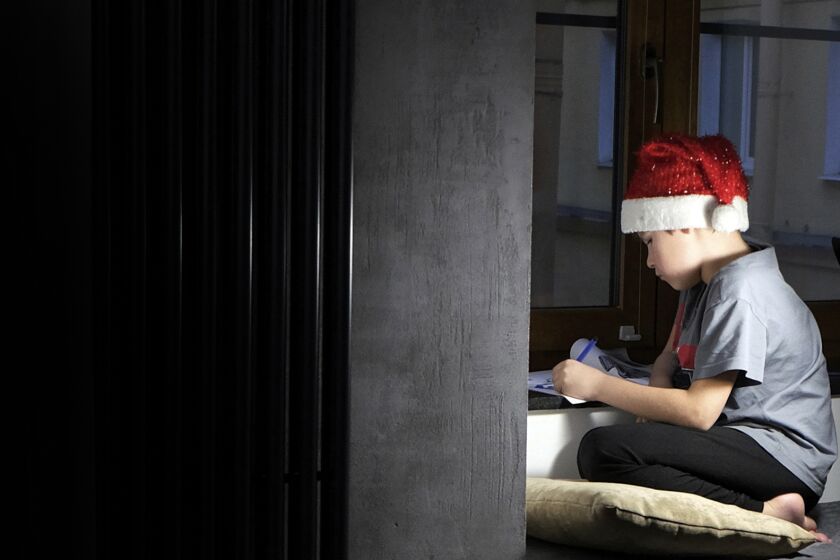 Boy wearing a Santa hat writes a letter asking for a gift for Christmas in a dark room.
