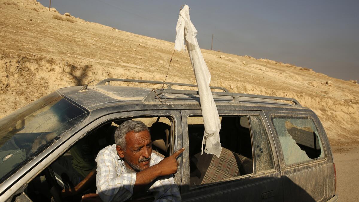 A man flying a white flag with his rear window shattered, is stopped on the road from Salhyia to Qayarrah on Thursday.