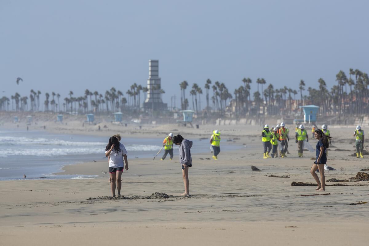Visitors play in the sand as a group of waste management personnel clean the beach at Huntington Beach on Monday.