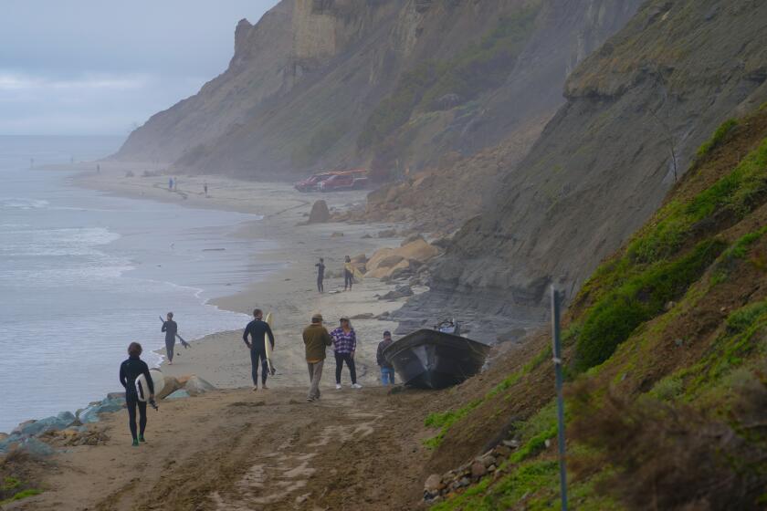San Diego, CA - March 12: Beach goers and surfers walk pass two pangas believed to have been used when two suspected smuggling boats overturned in the ocean off Black’s Beach in the Torrey Pines. At least eight people died late Saturday night when two suspected smuggling boats overturned in the ocean off Black’s Beach in the Torrey Pines. (Nelvin C. Cepeda / The San Diego Union-Tribune)