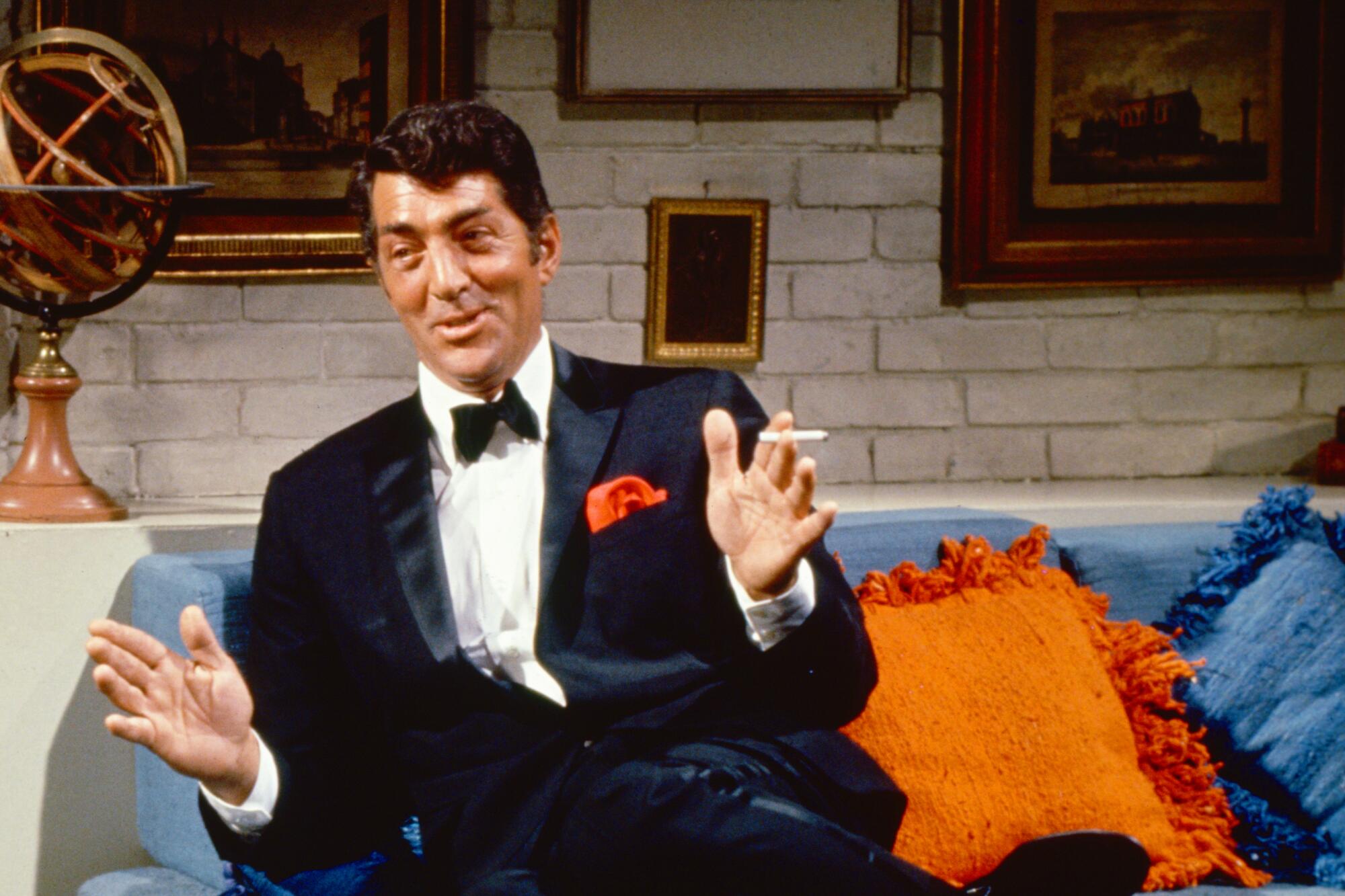 A man in a tuxedo lounges on a blue sofa