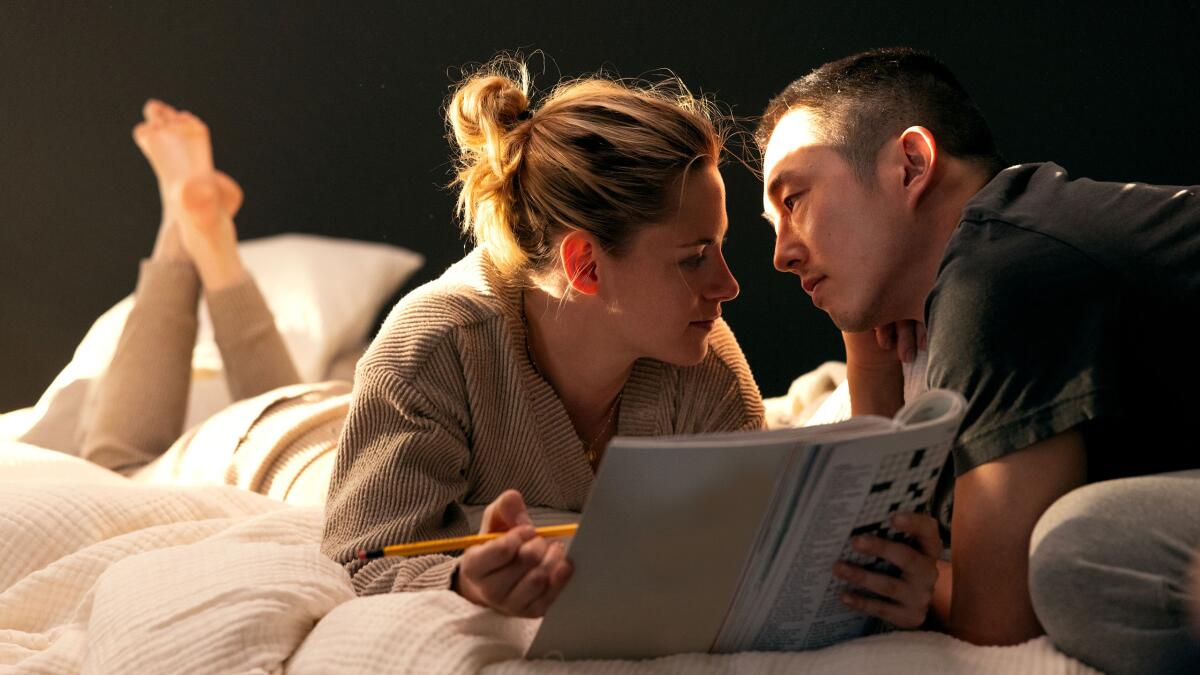 A woman and a man lie on a bed and stare at each other.