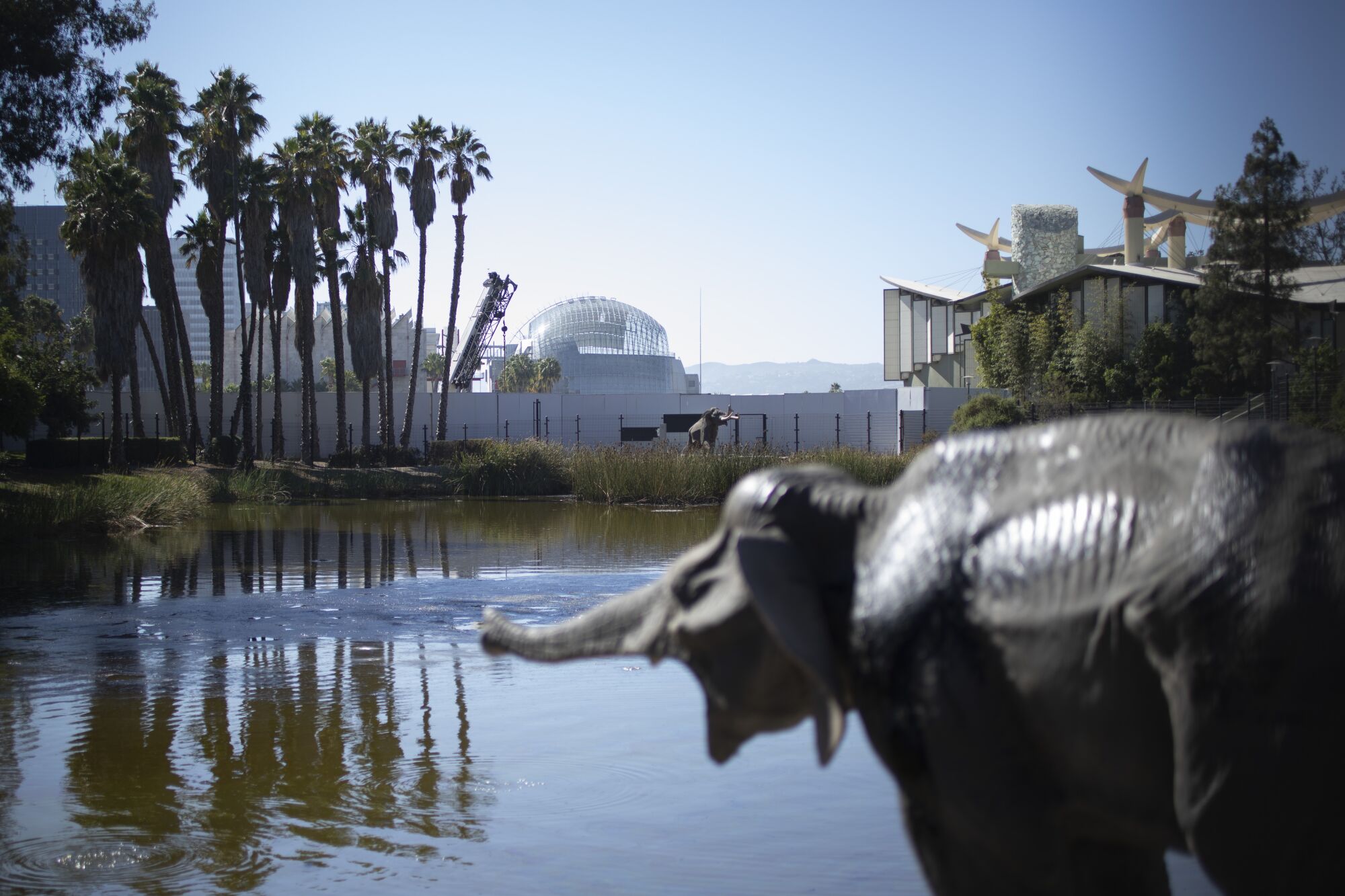 The spherical form of the Geffen Theater is seen in the distance, beyond the Lake Pit and a sculpture of a baby mammoth