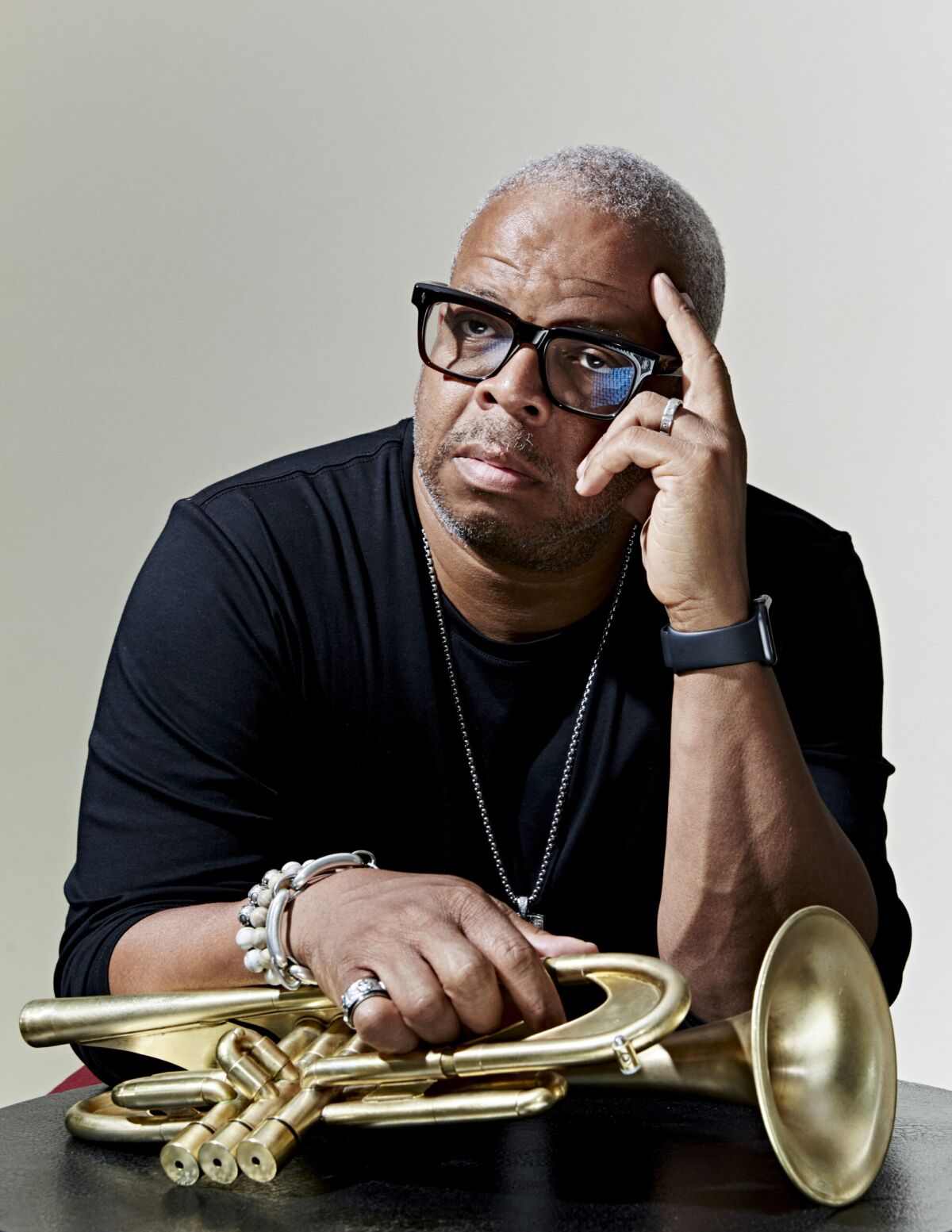 A seated man with one hand to his forehead and the other resting on a trumpet on a table in front of him