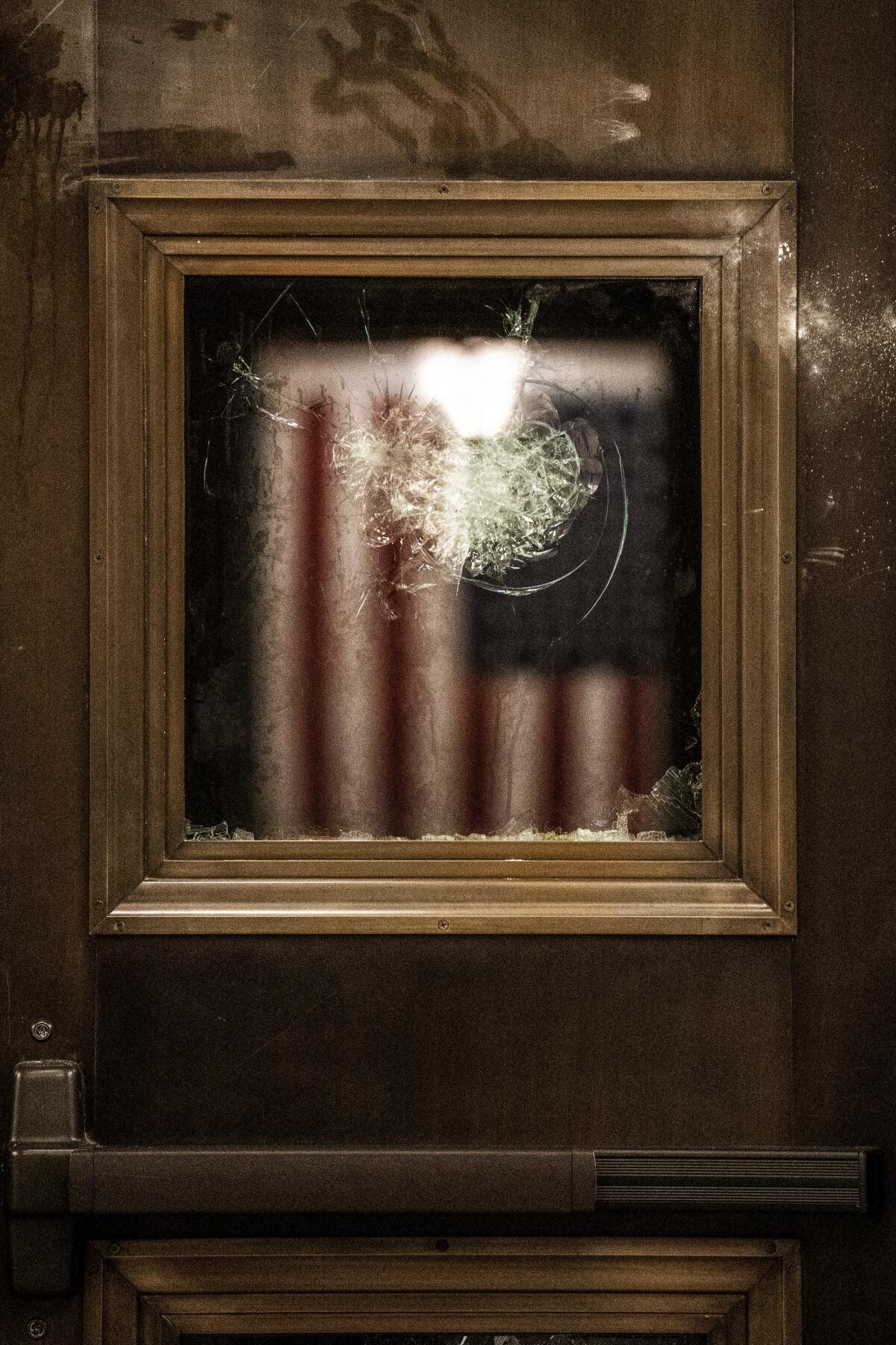 The reflection of an American flag in smashed glass at the Capitol.