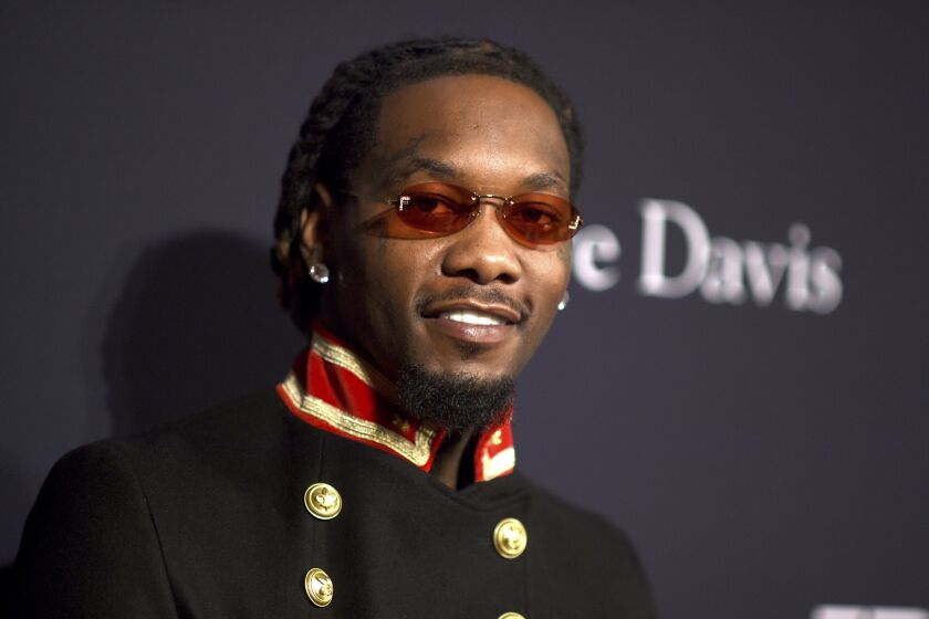 Offset smiles while wearing tinted red glasses, earrings and a jacket with gold buttons and a red collar.