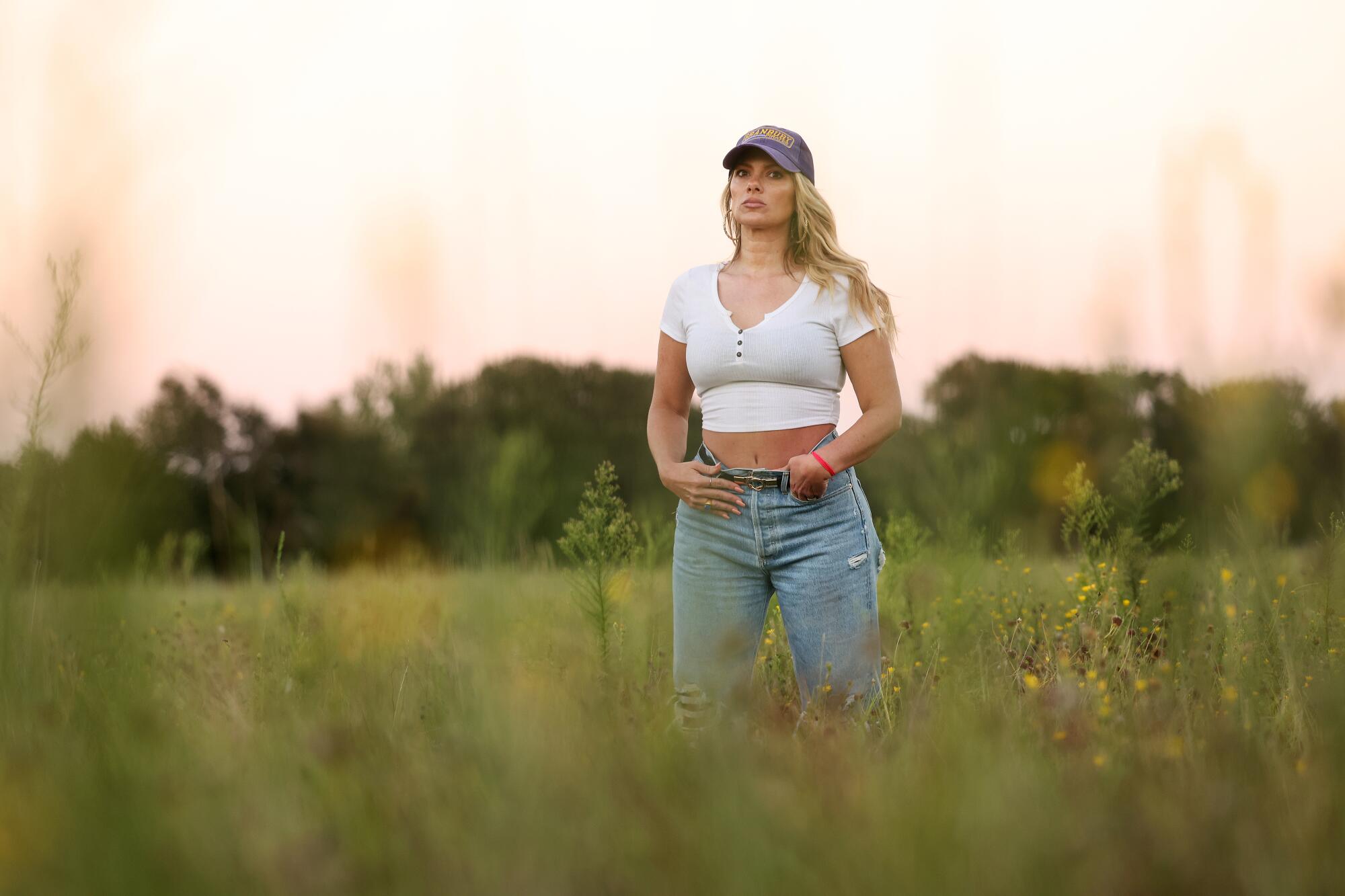 A woman wearing a cap stands in a field, staring into the distance