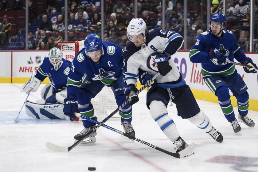 Vancouver Canucks' Bo Horvat (53) checks Winnipeg Jets' Mark Scheifele (55) during the first period of an NHL hockey game Friday, Dec. 10, 2021, in Vancouver, British Columbia. (Darryl Dyck/The Canadian Press via AP)