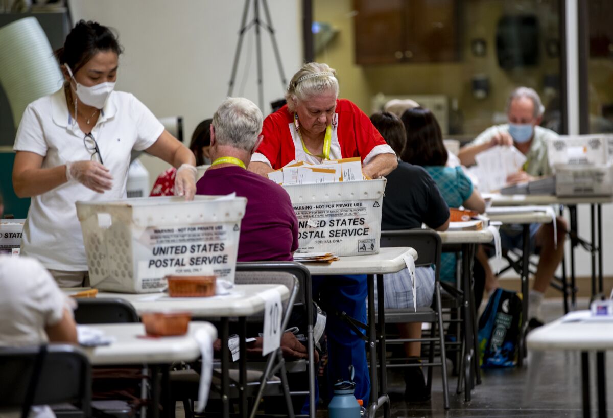 Election workers at the Orange County Registrar's office in Santa Ana sit or stand at tables to organize ballots.